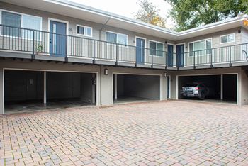 A car is parked in the garage of a two-story apartment building.